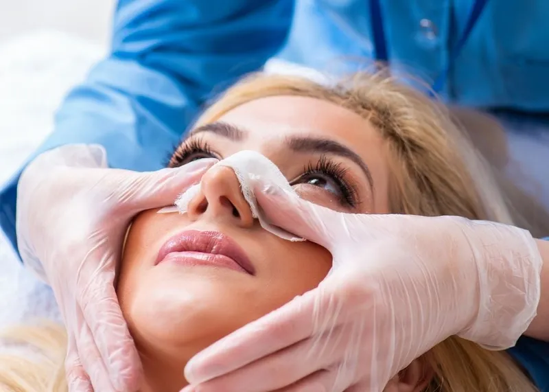 Surgeon examining a patient's nose during a rhinoplasty consultation.