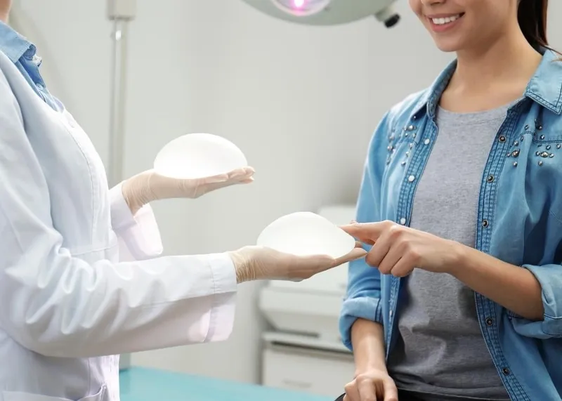 A plastic surgeon presents different silicone breast implant sizes and shapes to a patient during a pre-surgery consultation.