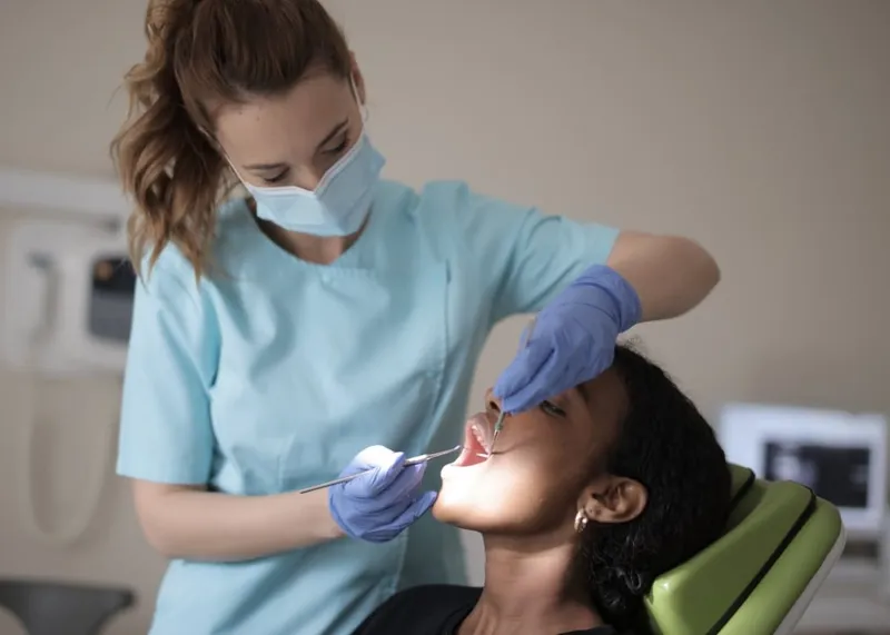 A dentist holds a dental implant model while explaining brand options to a patient.